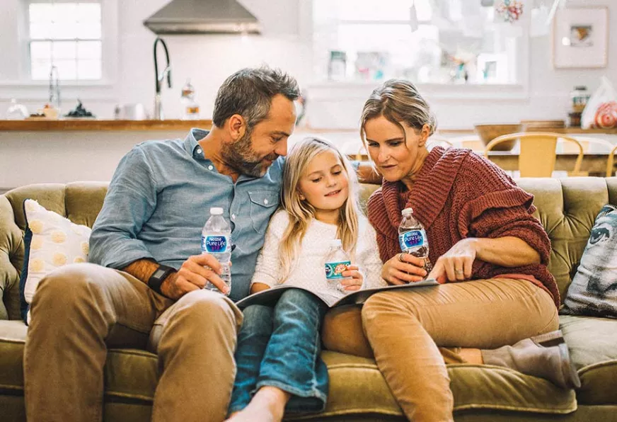 family reading book on couch together while drinking bottles of nestle pure life purified water
